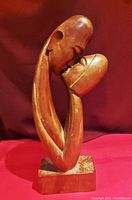 Front view of the hand carved wooden sculpture showing two abstract human figures embracing, with smooth curved lines and warm brown finish.