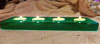 Green glass tea light candle holder holding four lit tea lights