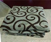 Folded gray plush throw with black spirals on a light-colored knitted surface.