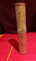Full view of carved bamboo rainstick standing vertically next to pencil for scale.