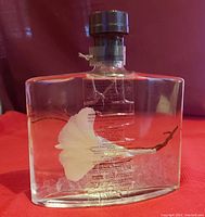 Front view of clear glass rectangular bottle with white flower trapped inside oil and text printed on bottle.