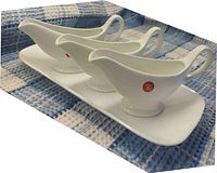 Three white porcelain soupcons arranged on white rectangular serving tray with raised edges on a blue and white checkered cloth.