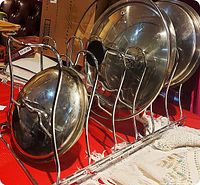 Side angle showing stainless steel rack holding pot lids upright in individual slots, with wire-frame curved dividers and sliding bottom.