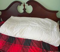White thick duvet folded on a bed with a dark wood headboard, showing part of quilted stitching and fabric texture.