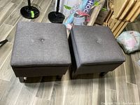 Two square charcoal fabric storage ottomans with tufted tops viewed from above, placed on a tiled floor.