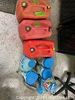 Three red plastic gas containers arranged on floor, visible wear, with six blue-capped containers of de-icer salt liquid placed in a grey storage bin below them.