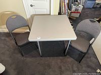 Two padded folding chairs displaying brown woven fabric upholstery flanking a square plastic card table.