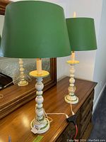 Pair of 1970s vintage table lamps with green spindle-style bases and green shades on wooden dresser in front of mirror.