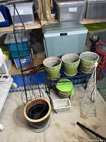 Photo of assorted garden pots on black metal stand with compost container and iron trellises around