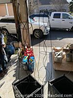 Two tall metal trellises placed inside two black square planter boxes in garage setting with various other items visible around.