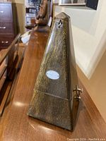 Side view of pyramid-shaped wooden metronome with visible wood grain and metal plaque on front.