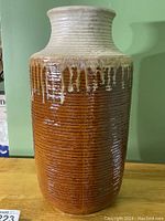 Front view of a tall ceramic vase with textured brown glaze and beige drip glaze near the top.