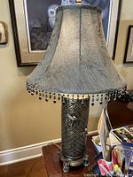 Full view of the table lamp showing the metal base and fabric lampshade with tassel fringe
