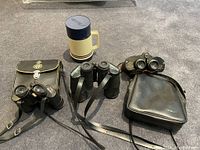 Photo showing all items: three binoculars (one larger pair, two smaller pairs) with carrying cases and the vintage Aladdin insulated flask mug.