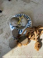 Lot showing brass propeller, metal buoys, white life ring, and coiled rope on concrete floor