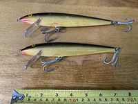 Top-down photo of two Rapala #18 Magnum Floater fishing lures placed side by side next to a measuring tape showing length around 8 inches.
