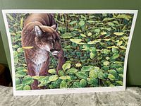 Full view of signed and numbered poster showing cougar in foliage with water droplets on leaves