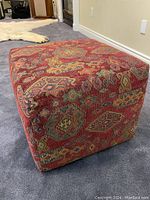 Overall view of vintage kilim rug upholstered ottoman showing red geometric patterned fabric and cube shape.