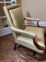 Side angle showing the tan leather upholstery, studded nailhead trim, wooden armrest and leg design on wood floor