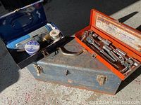 Three metal tool boxes, one large blue with latches, one small blue with plumbing parts, and one orange with socket tools.