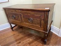 Full frontal view of the walnut blanket box on wooden stand with cast iron wood wheels.