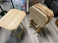 Four wooden folding TV tables, three stacked folded and one assembled and standing.