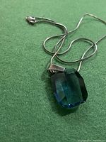 Full length view of silver chain with blue stone pendant on green background.