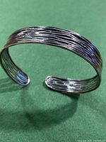 Close-up front angle view of the open cuff bracelet showing textured linear silver pattern and polished finish.