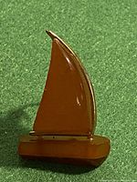 Front view showing sailboat-shaped brooch with Baltic amber sail and base on green fabric.