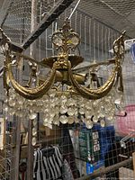 View of the full brass chandelier showing ornate design, crystal prisms hanging from frame, and light socket bulbs, some crystals missing.