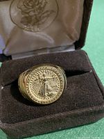 Front view of ring in presentation case showing raised Liberty coin design