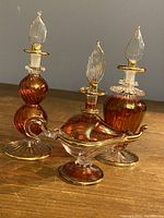 Front view of three vintage cranberry glass miniature perfume bottles with clear glass stoppers and gold inlay details.