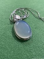 Close-up photo of moonstone oval pendant showing translucent and polished surface with silver-tone bezel.