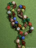 Full view of vintage Murano glass bead necklace showing multicolored swirled beads and metal dividers, coiled on a green background.
