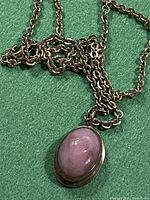Close-up photo showing oval iridescent pink stone in gold-tone bezel pendant on green background.