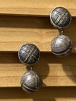 Pair of vintage silver tone clip-on earrings lying on wooden surface showing textured crosshatch pattern on circular segments.