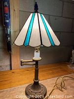 Front view of the vintage stained glass swivel lamp on a wooden surface, showing the stained glass shade with turquoise and white panels and the decorative metal base.