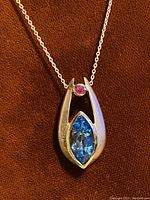 Close-up of the vintage sterling pendant showing blue marquise cut stone and round red stone, hanging on a silver chain against a brown background.