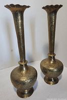 Two tall brass vases with scalloped rims and detailed engraved floral designs, one with bulbous base, one with slightly elongated base