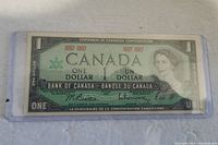 Front side of Canadian 1967 one dollar bill in protective plastic showing portrait of Queen Elizabeth II and centennial dates