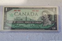 Front side of the 1967 Canadian 1 dollar bill in protective sleeve showing portraits, denomination, and signatures.