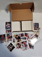 Full open box with several stacks of hockey cards and some cards spread on the surface showing players from different teams in action.