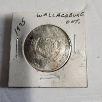 Silver Canadian Centennial Dollar coin with Wallaceburg Ontario commemorative design in a white cardboard holder.