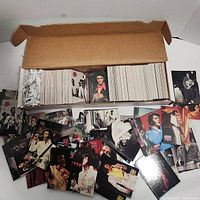 Photo showing a large number of Elvis Presley cards arranged inside and outside a cardboard box. The cards depict Elvis in various outfits and poses.