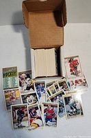 Open cardboard box containing a large stack of hockey cards with several individual cards laid out showing various professional hockey players.