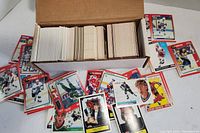 Cardboard box filled with three stacks of hockey cards and several cards displayed around the box showing front designs of various hockey players.