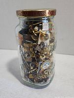 Side view of a glass jar filled with various decorative pins inside.