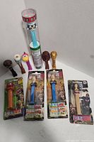 Photo showing 11 Pez dispensers including one in a clear tube, several loose with character heads, and five sealed in packaging featuring various character designs.