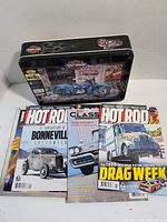 Photo showing the closed metal tin with Harley-Davidson motorcycle puzzle illustration and three Hot Rod magazines laid out in front.