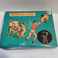 Top view of the Basketball Player toy box showing painted illustrations of basketball players and a hoop. Box edges show wear and slight damage.